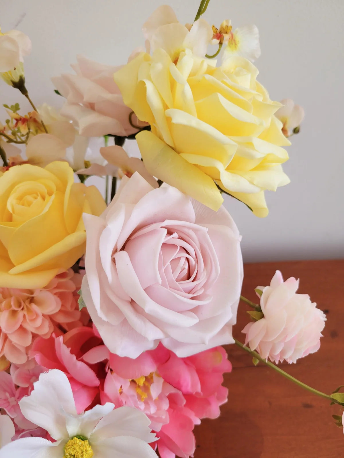 Bouquet of yellow, pink, and white flowers on a wooden surface with a light background