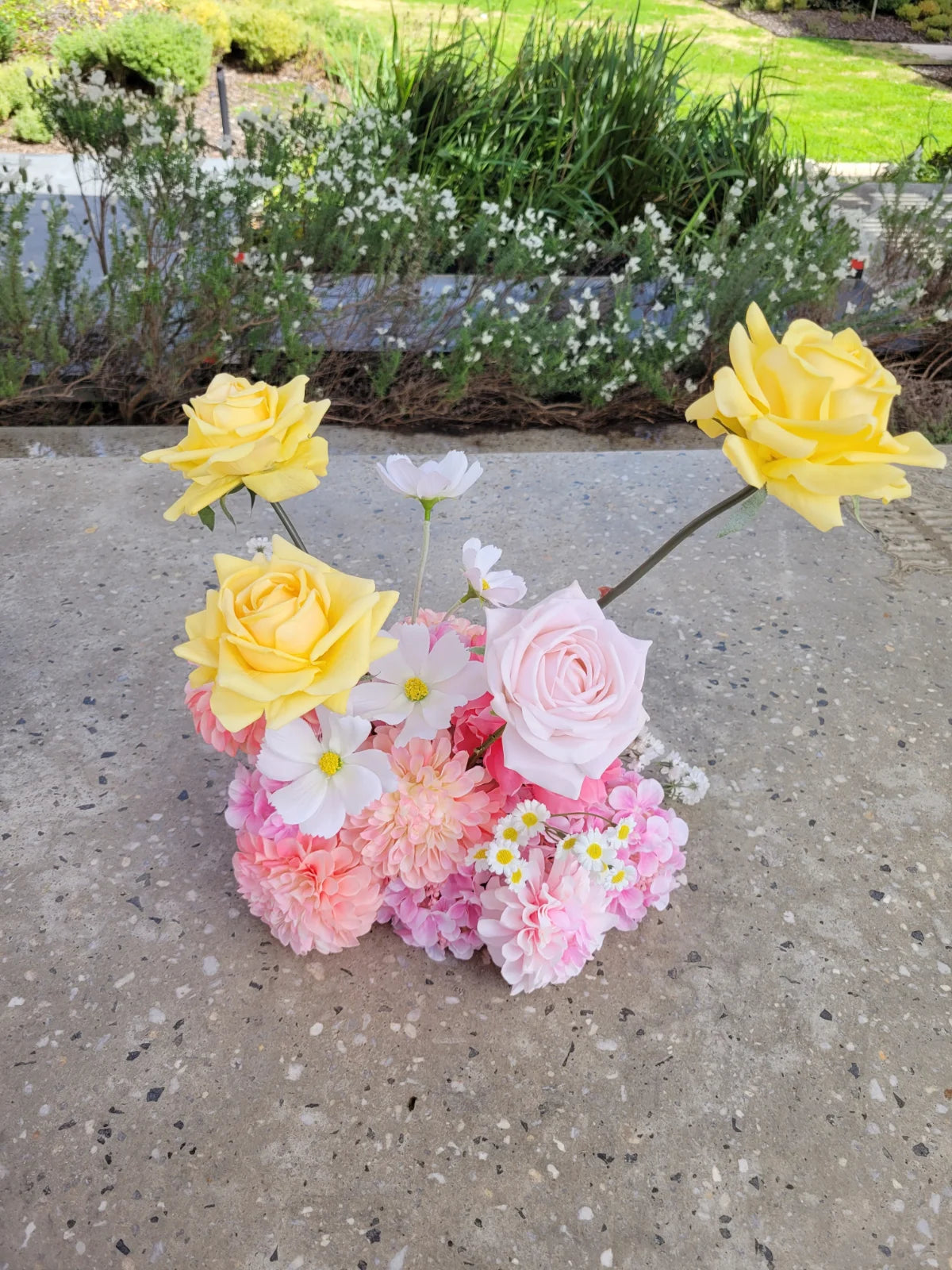 Heart-shaped arrangement of flowers on a concrete surface with a garden background