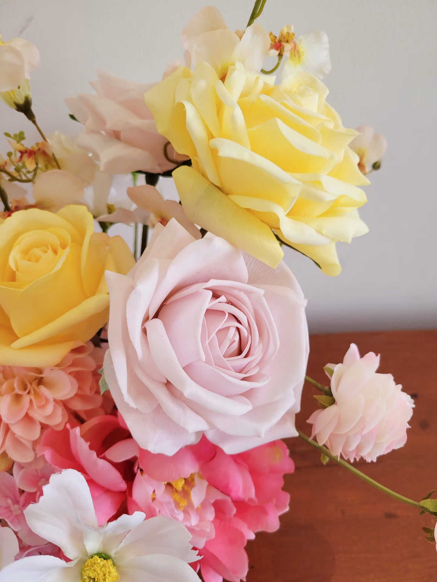 Side view of a yellow real touch rose next to a blush pink rose