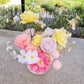 A cheerful yellow, pink and white faux flower arrangement on a bench outdoors
