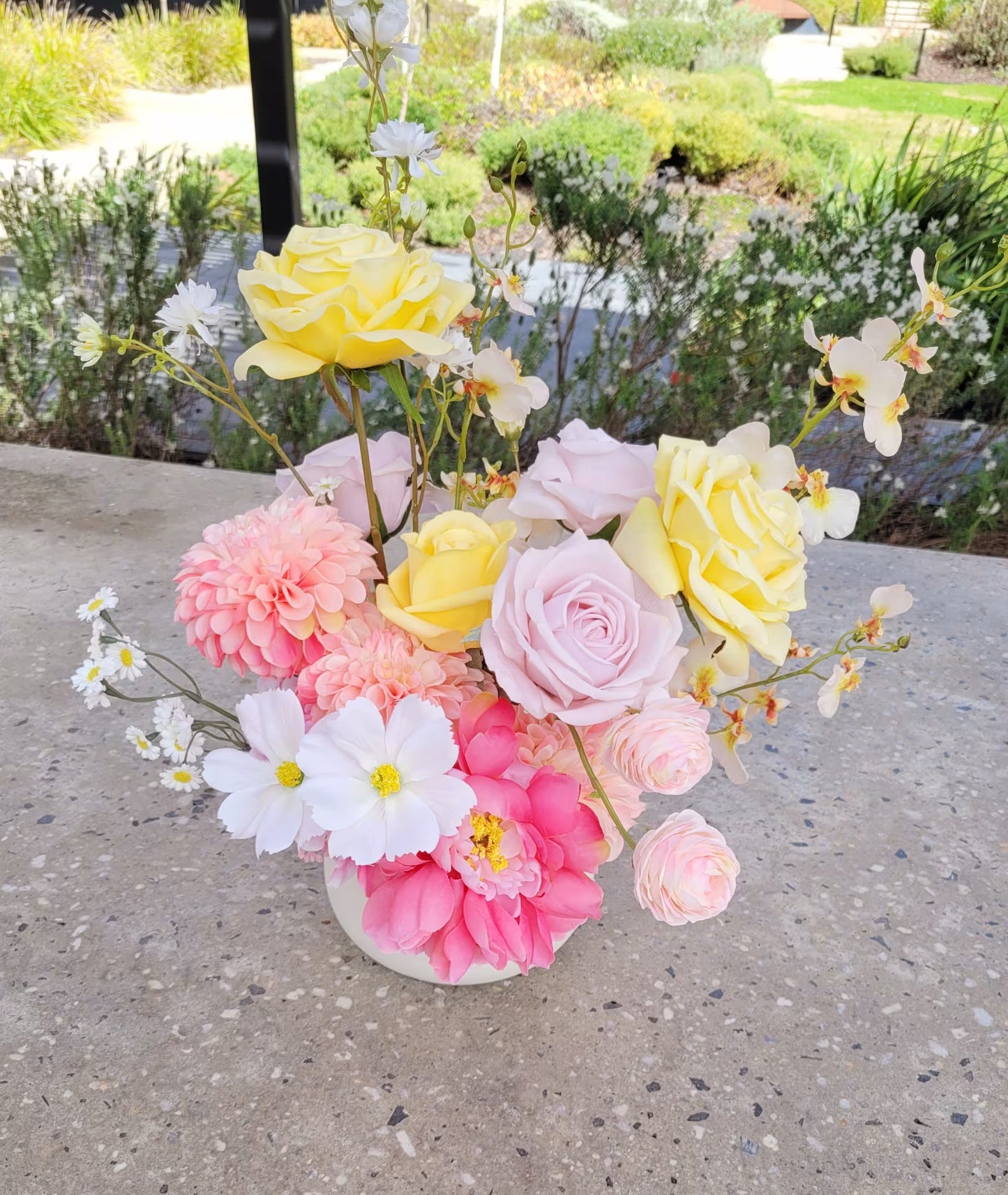 Floral arrangement with pink, yellow, and white flowers in a vase on a concrete surface.