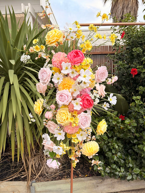 A wedding arbour artificial flower arrangement in pink, yellow and white in a garden setting