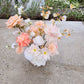 Artificial flower arrangement of peach and white tones on a concrete bench