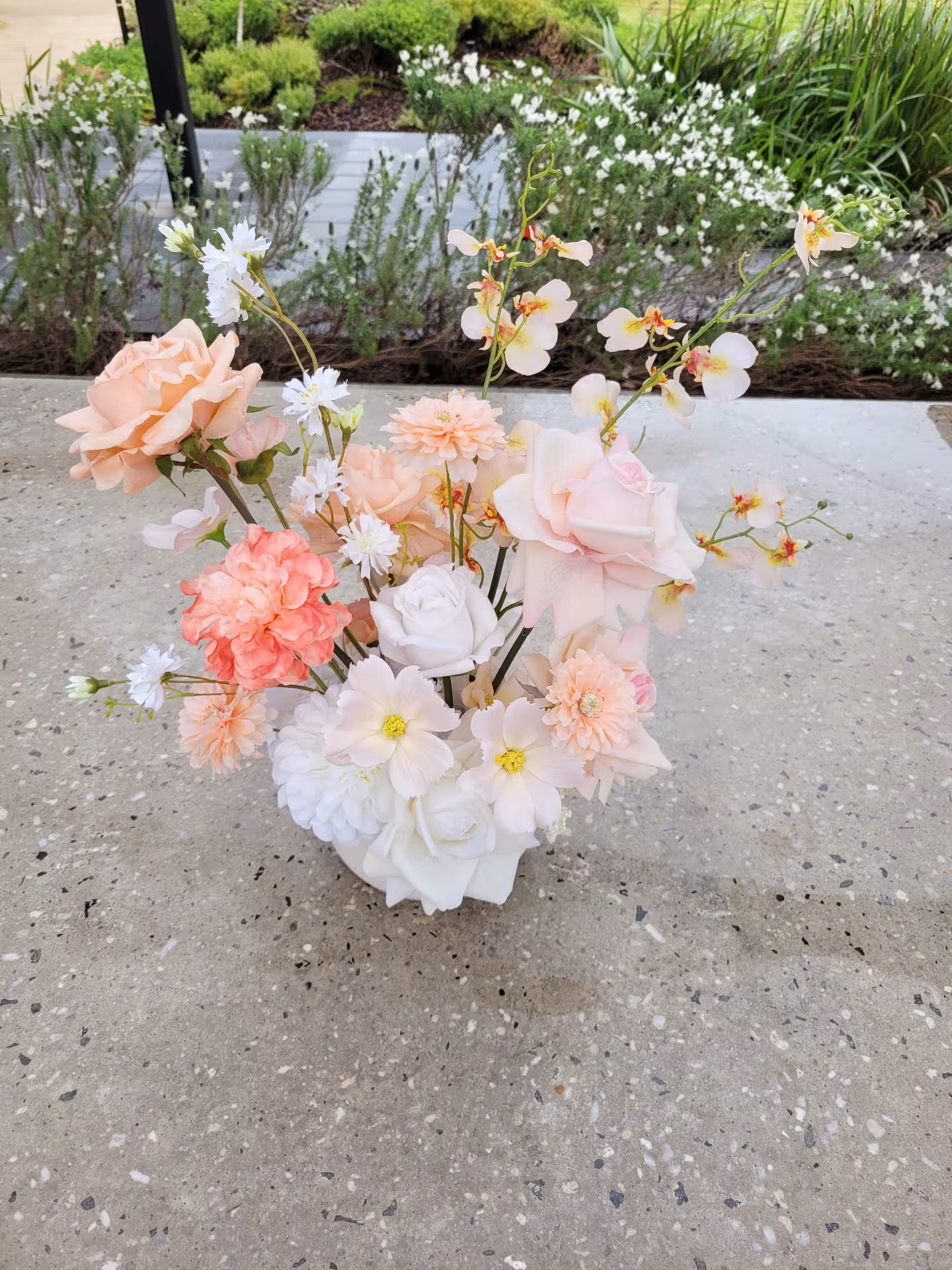 Artificial flower arrangement of peach and white tones on a concrete bench