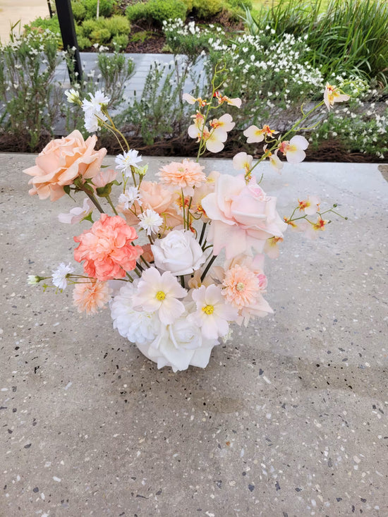Faux flower arrangement of peach and white tones on a concrete bench
