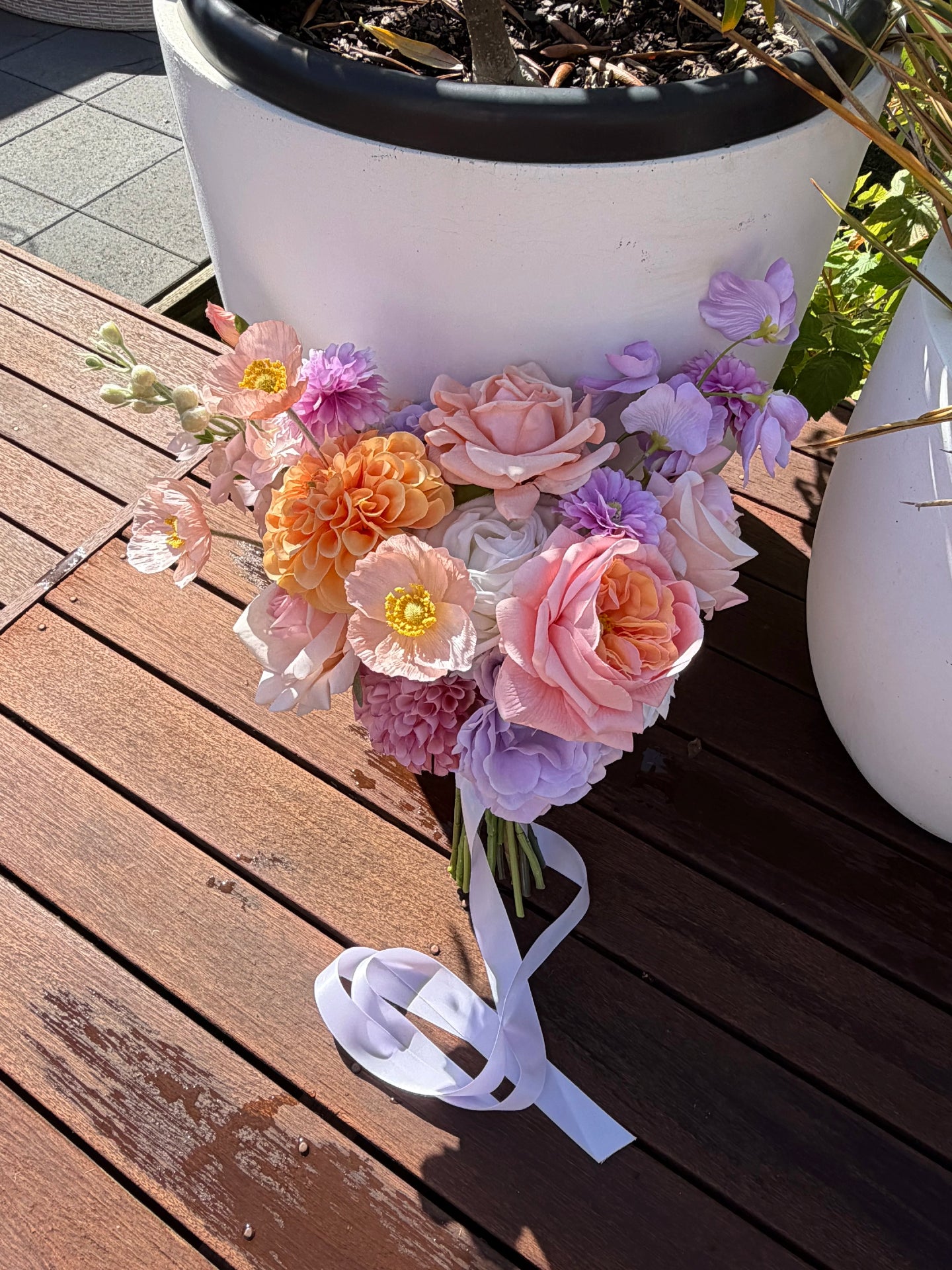 Artificial wedding bouquet of pastel flowers with a white ribbon on a wooden surface