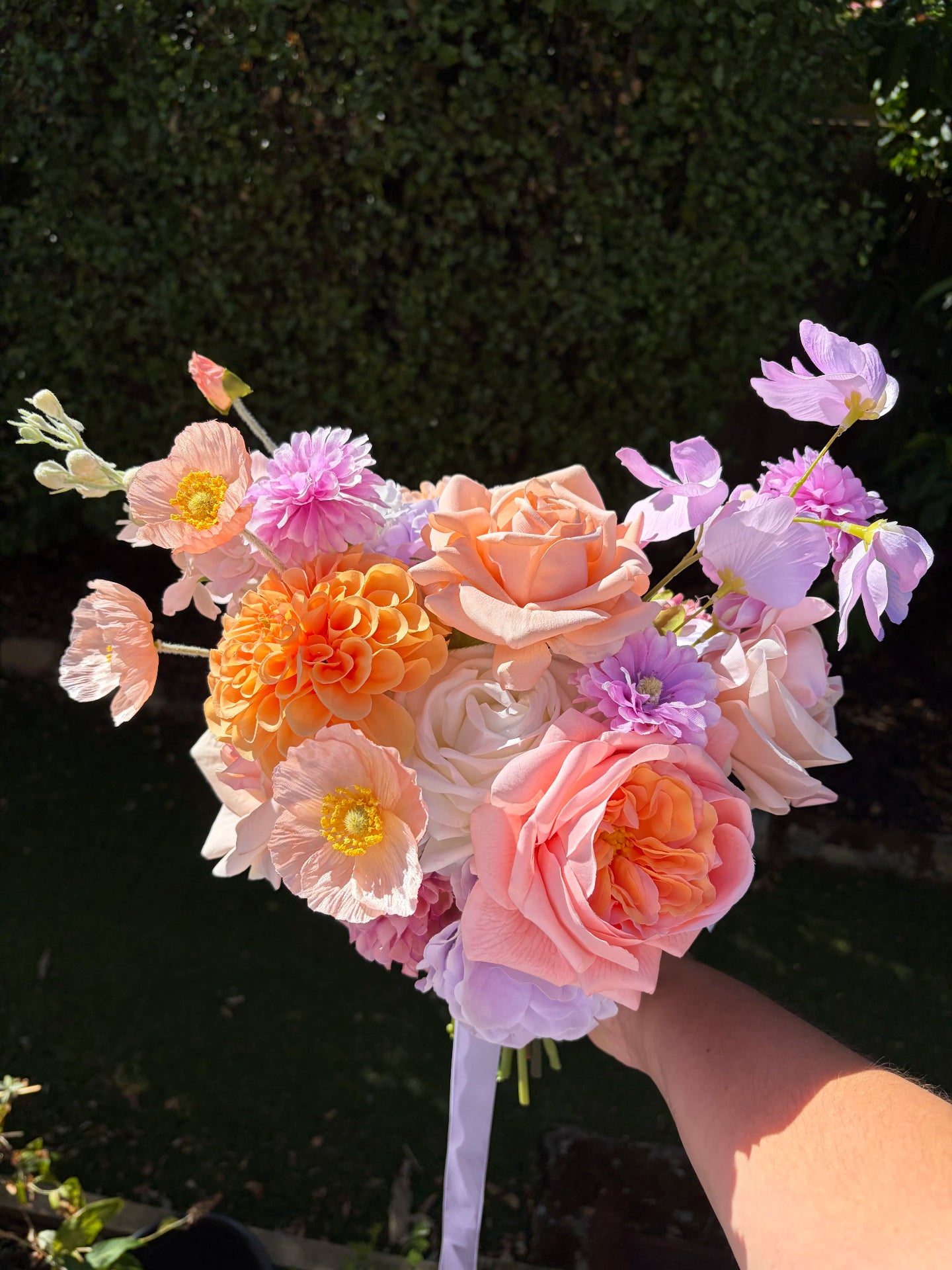 Artificial wedding bouquet of spring flowers held by a person against a dark green foliage background