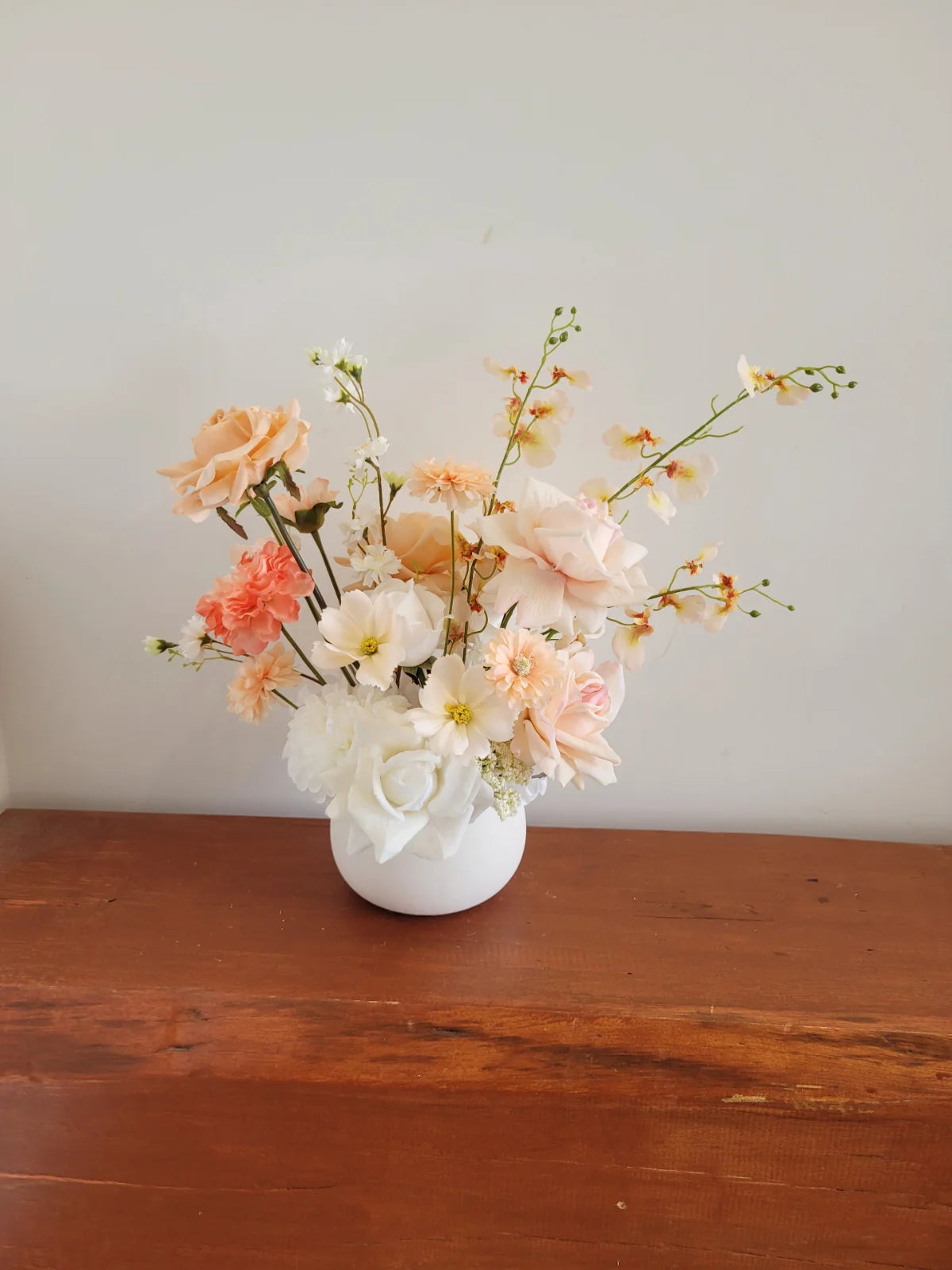 Floral arrangement in a white vase on a wooden surface with a plain background
