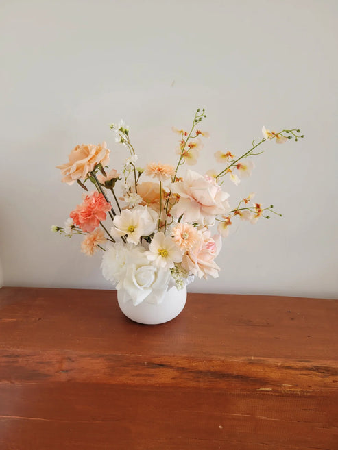 Floral arrangement in a white vase on a wooden surface with a plain background