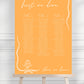 Orange wedding seating chart with text on a stand against a white background