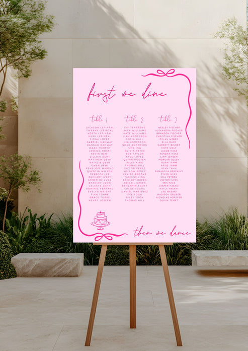 Pink seating chart on a wooden stand outdoors with plants and stone wall in the background