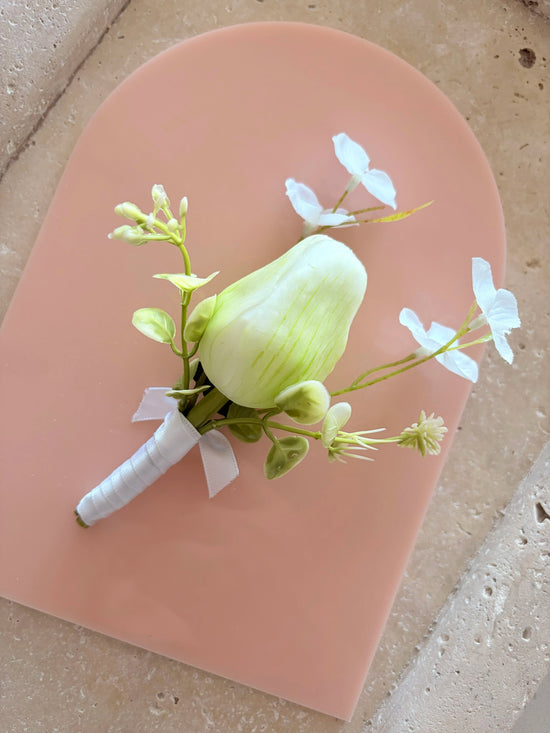white buttonhole with whimsical white wildflowers displayed on a peach acrylic arch for product photography