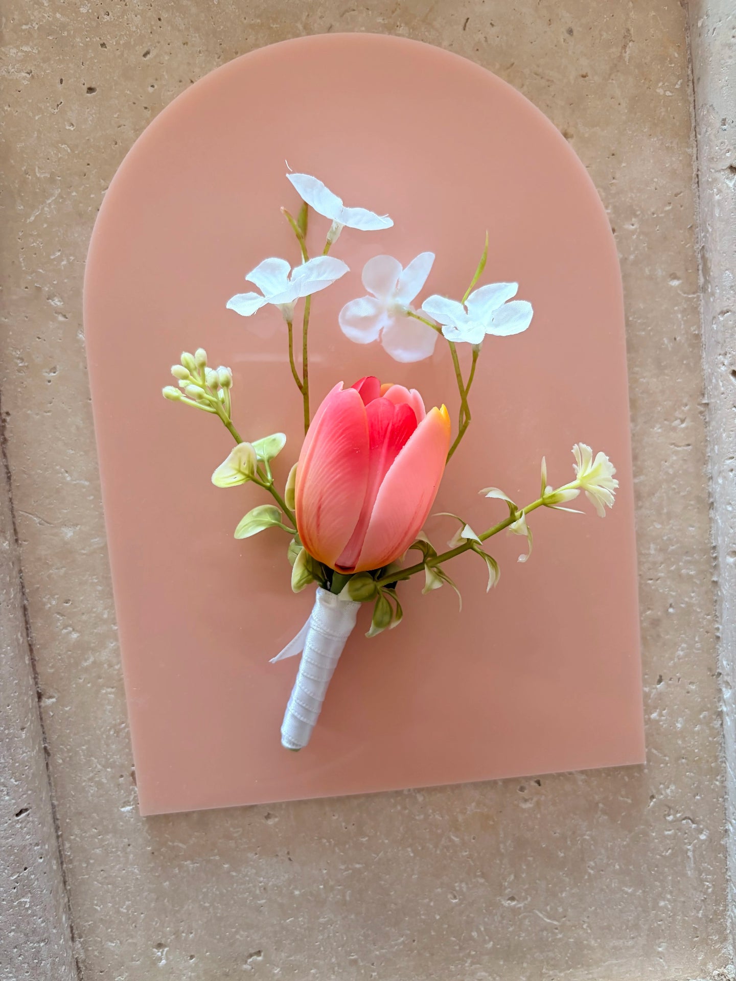 Pink buttonhole with whimsical white wildflowers displayed on a peach acrylic arch for product photography.