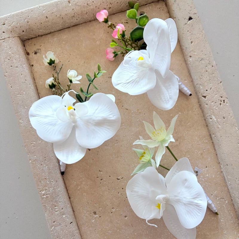 Set of white orchid buttonholes on a textured beige surface