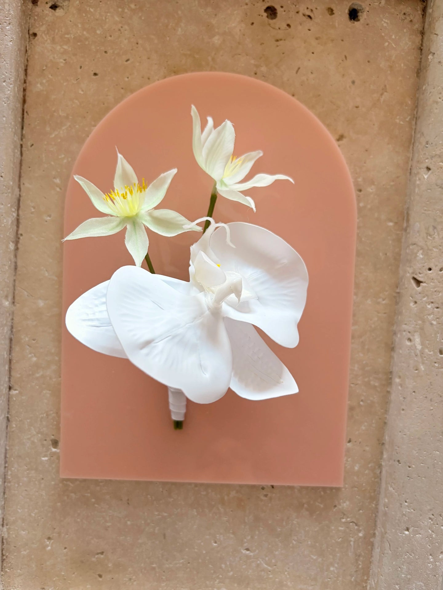 White orchid buttonhole displayed on a flat acrylic peach arch