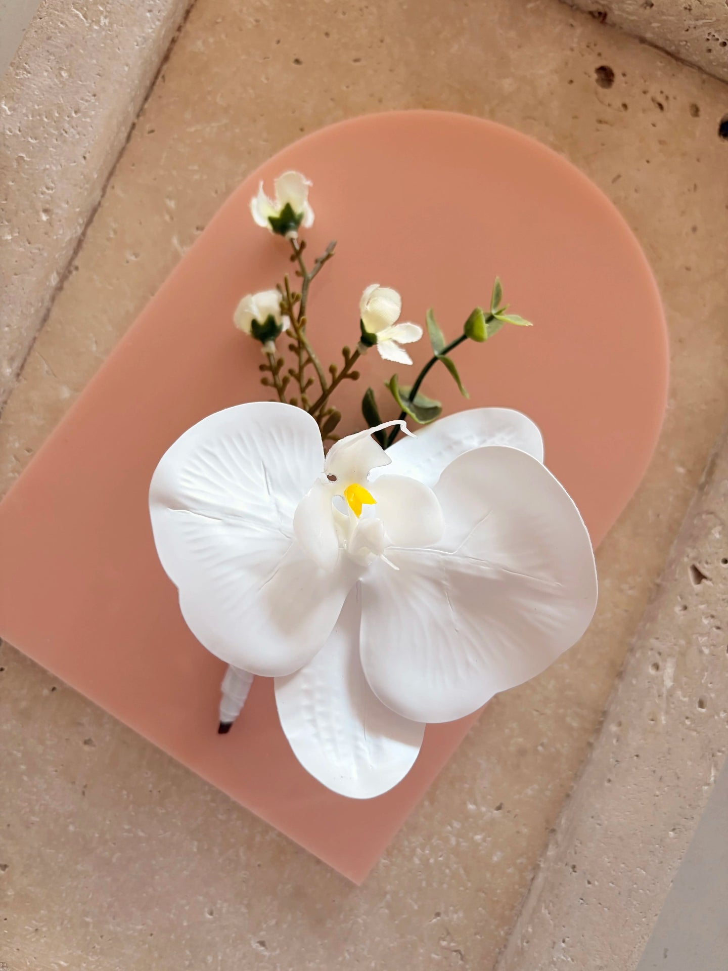 White orchid buttonhole displayed on a flat acrylic peach arch with small white flower detailing