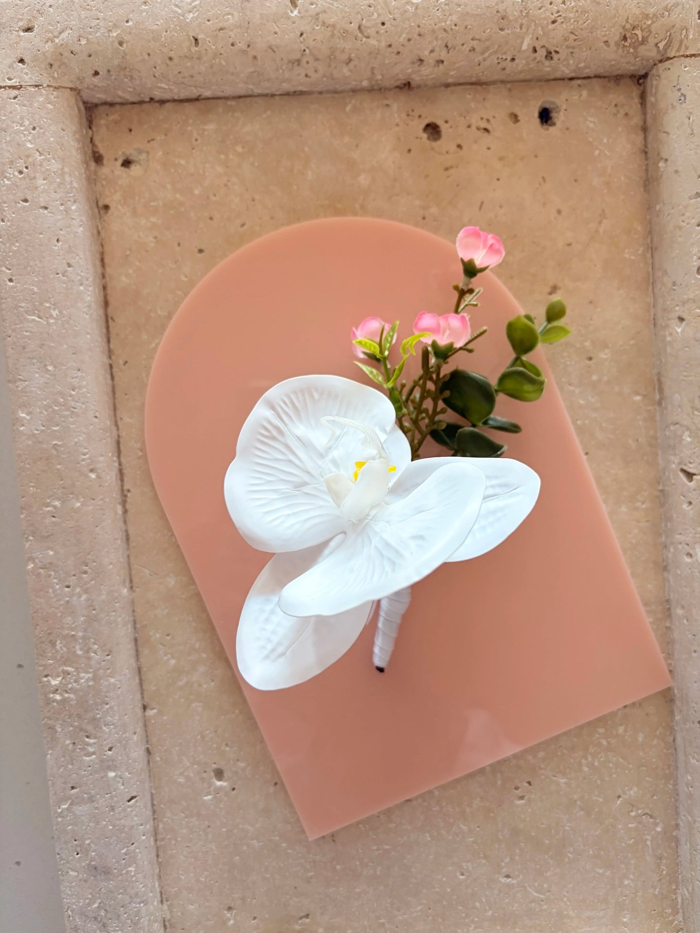 White orchid buttonhole displayed on a flat acrylic peach arch with small pink flower detailing
