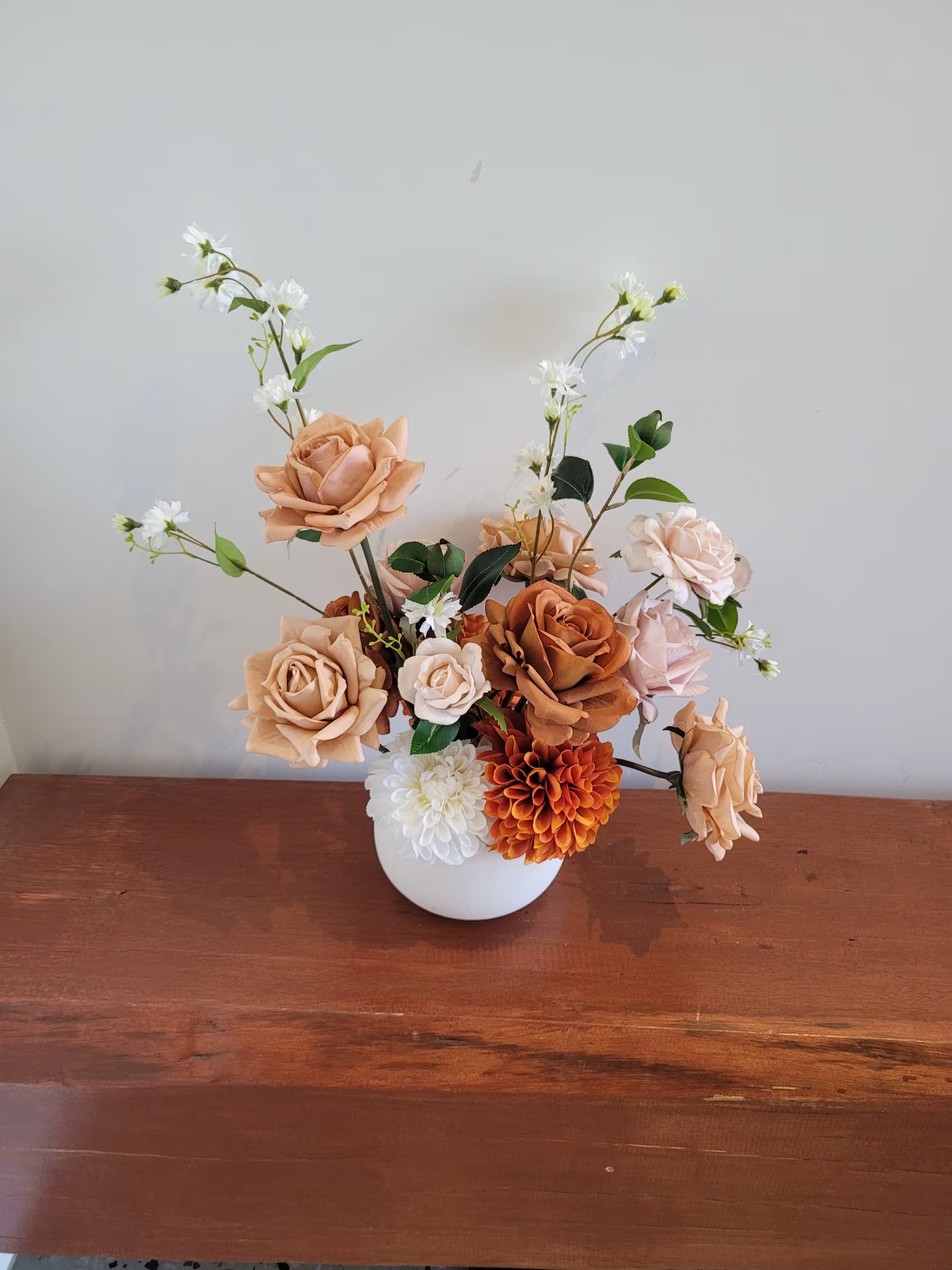 Rustic style artificial flower arrangement in a white pot on a wooden bench