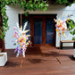 Two floral arrangements on stands in front of a building with glass doors with wooden deck and greenery.