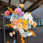 Colourful floral arrangement attached to a decorative stand with wooden beams and glass wall in the background.