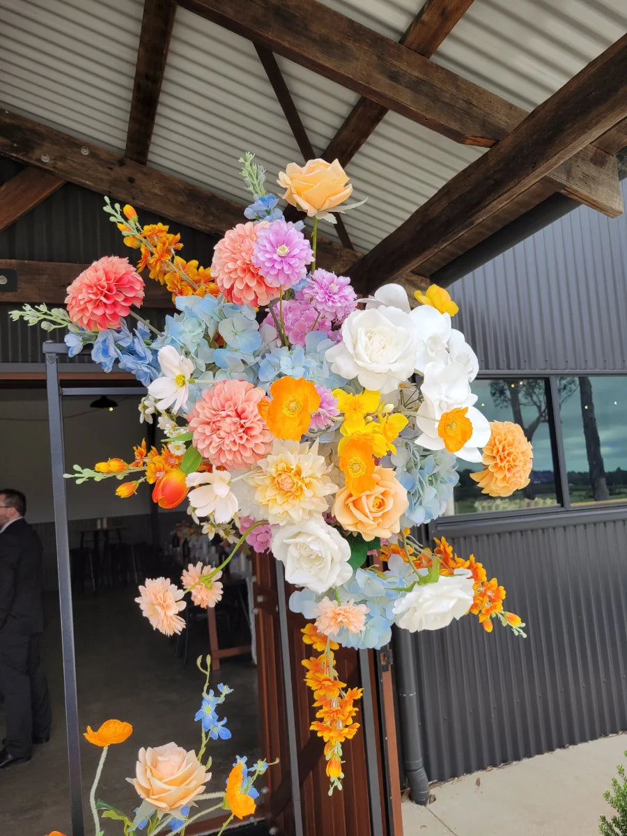 Colourful floral arrangement attached to a decorative stand with wooden beams and glass wall in the background.