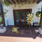 Decorative flowers on a wooden deck with a white wall and brown door in the background