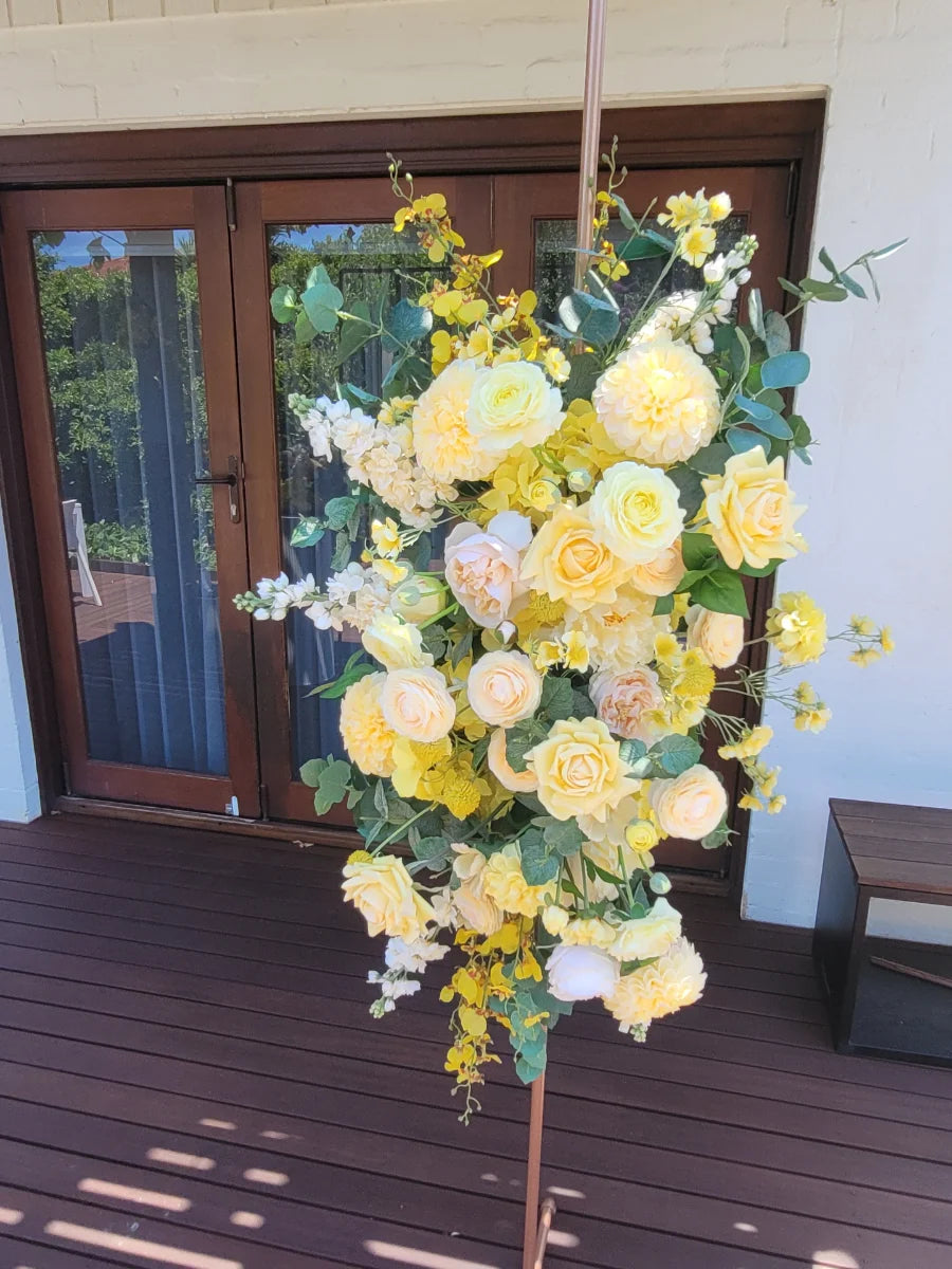 Floral arrangement with yellow and white flowers on a wooden deck.