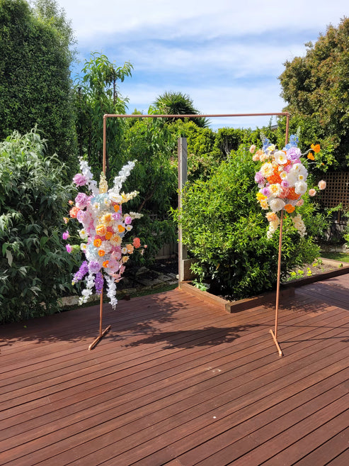 Two large arbour flower arrangements on a gold frame in a garden setting