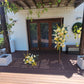 Yellow and green flowers on a wooden deck with a white wall and brown door in the background