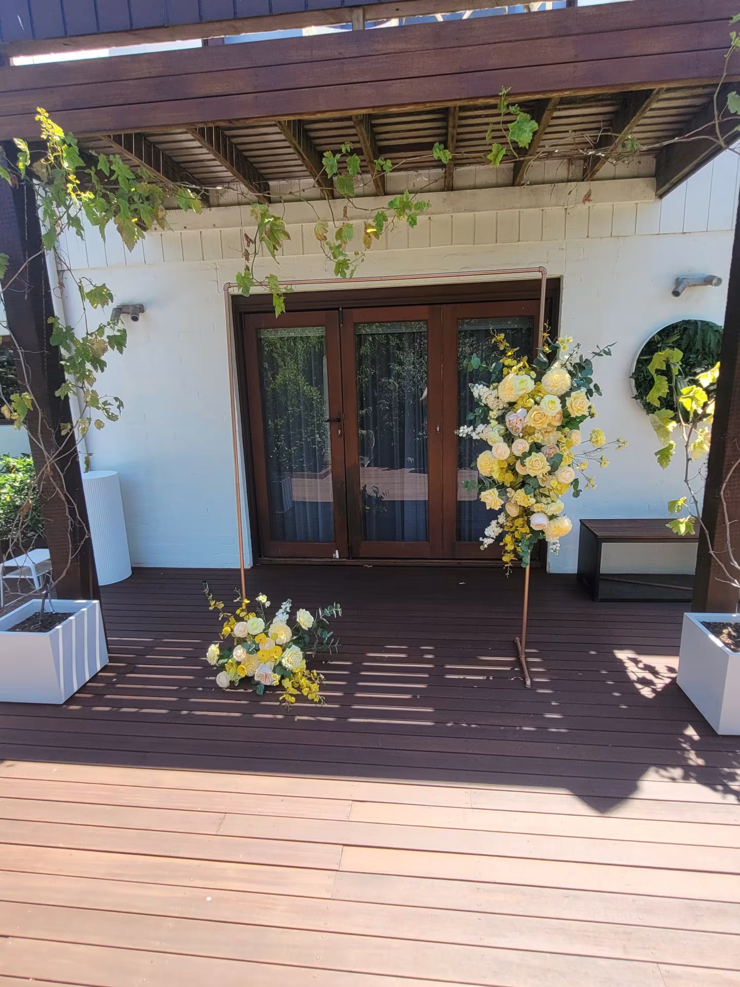 Yellow and green flowers on a wooden deck with a white wall and brown door in the background