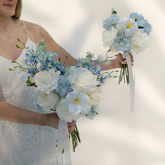 Woman holding two bouquets of white and blue flowers against a plain background