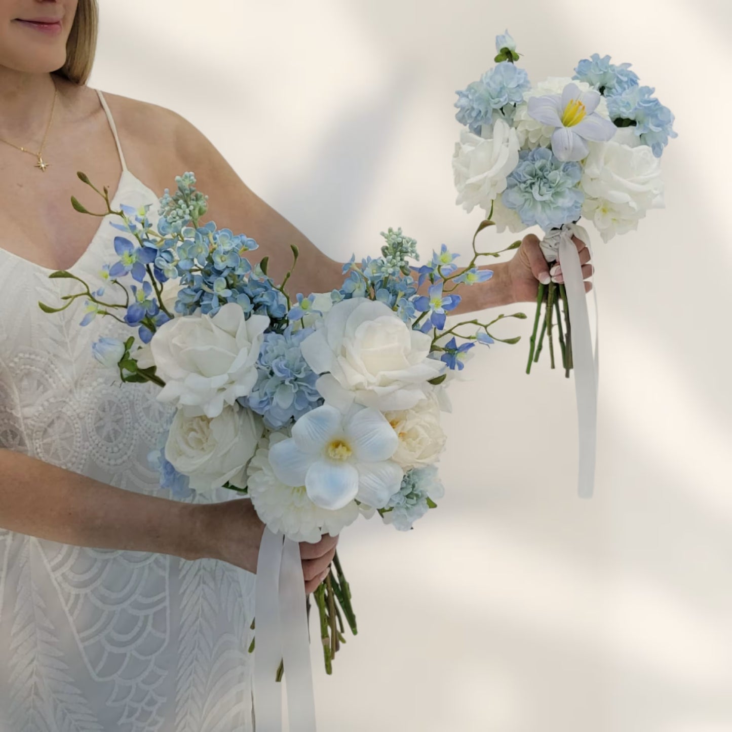 Woman holding two wedding bouquets of white and blue flowers against a plain background