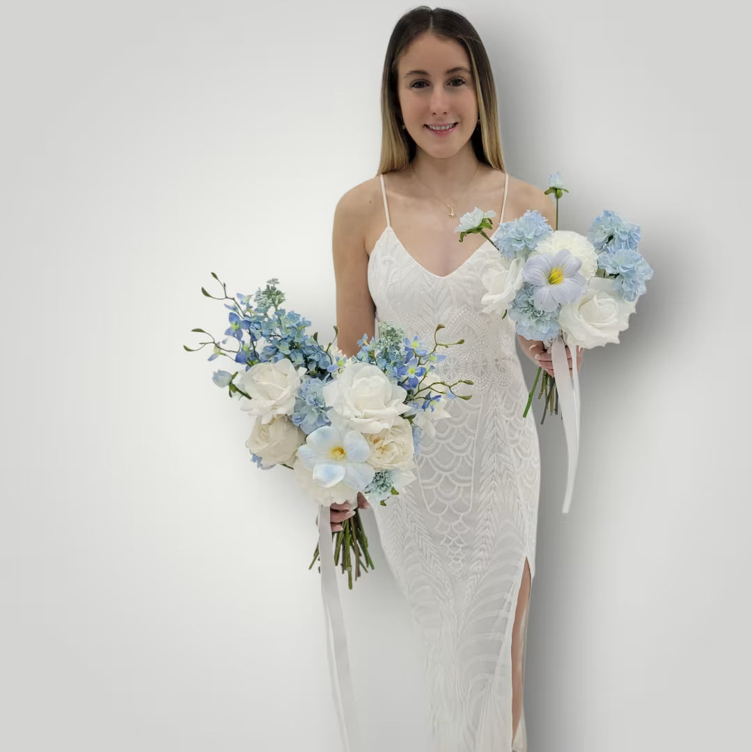 Woman in a white wedding dress holding multiple wedding bouquets against a plain background