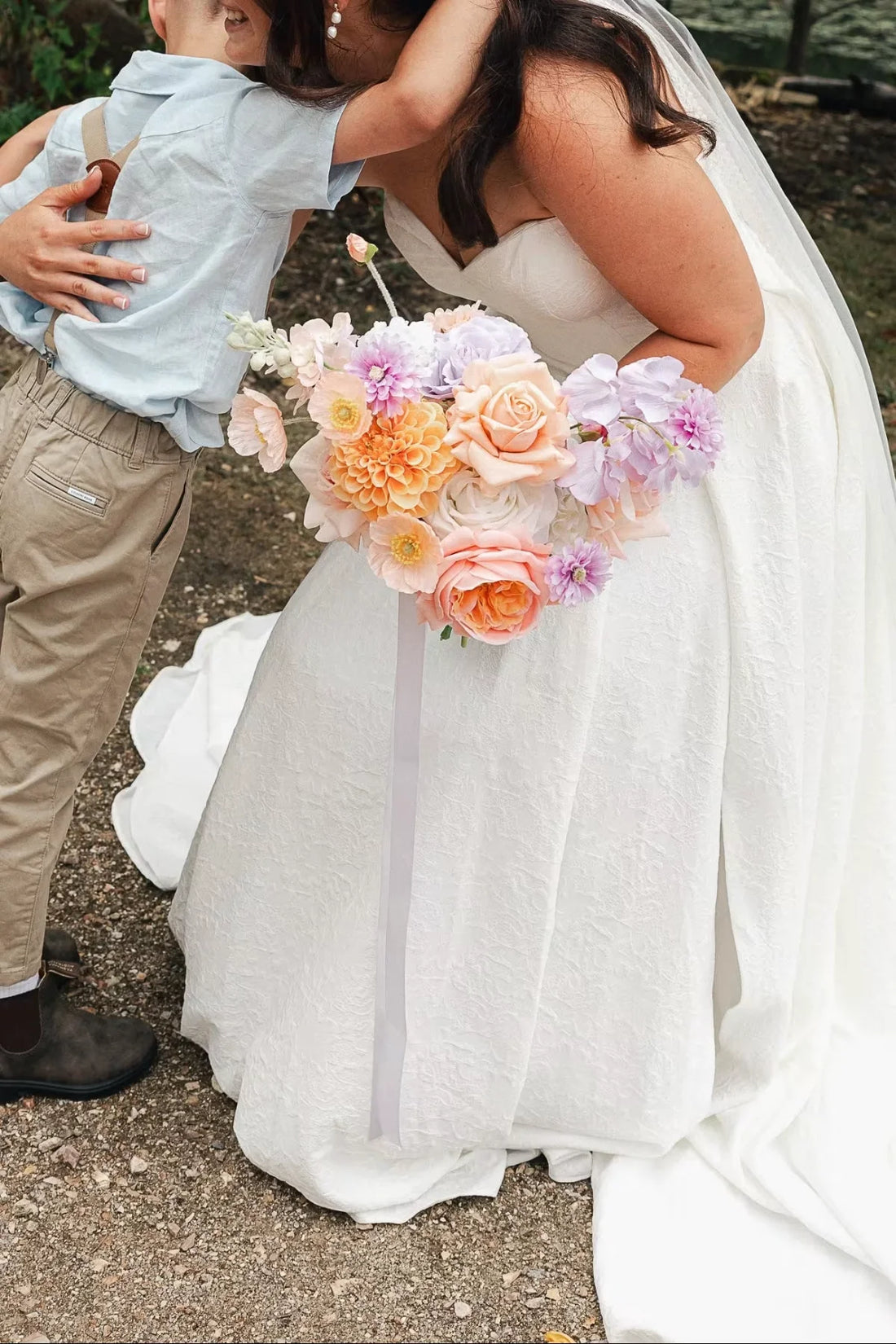 Bride and son hugging outdoors with a coloruful bouquet.