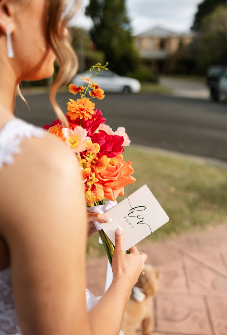 bride holding a bouquet of artificial wedding flowers with her vows on a street background