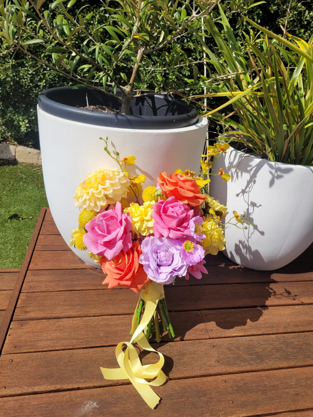 Bouquet of colorful flowers with a white planter and greenery in the background.