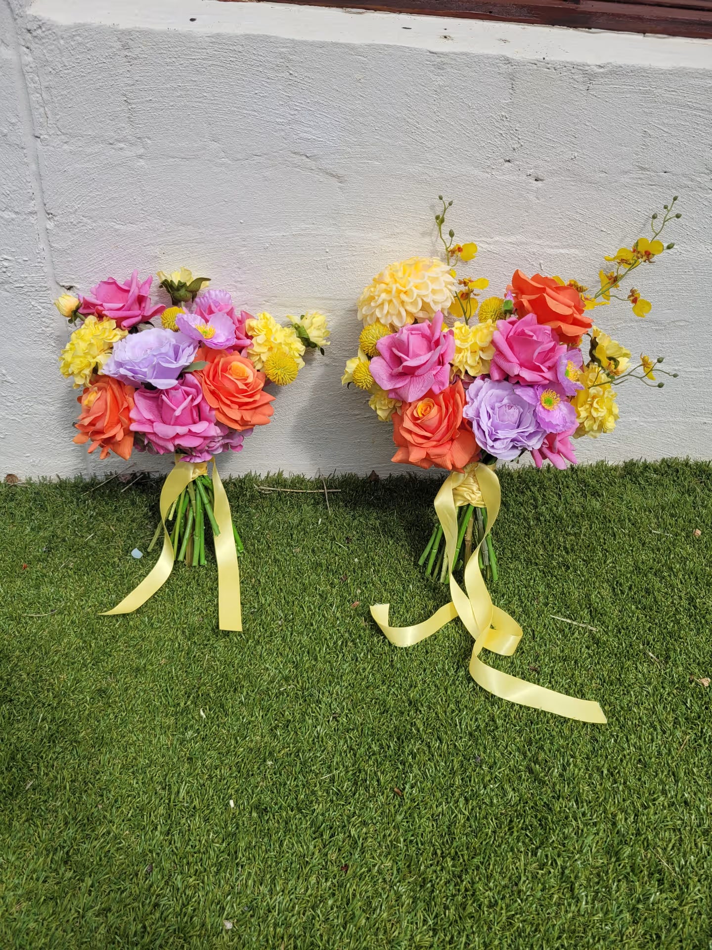 Two floral bouquets with colorful flowers and ribbons on a grassy surface.