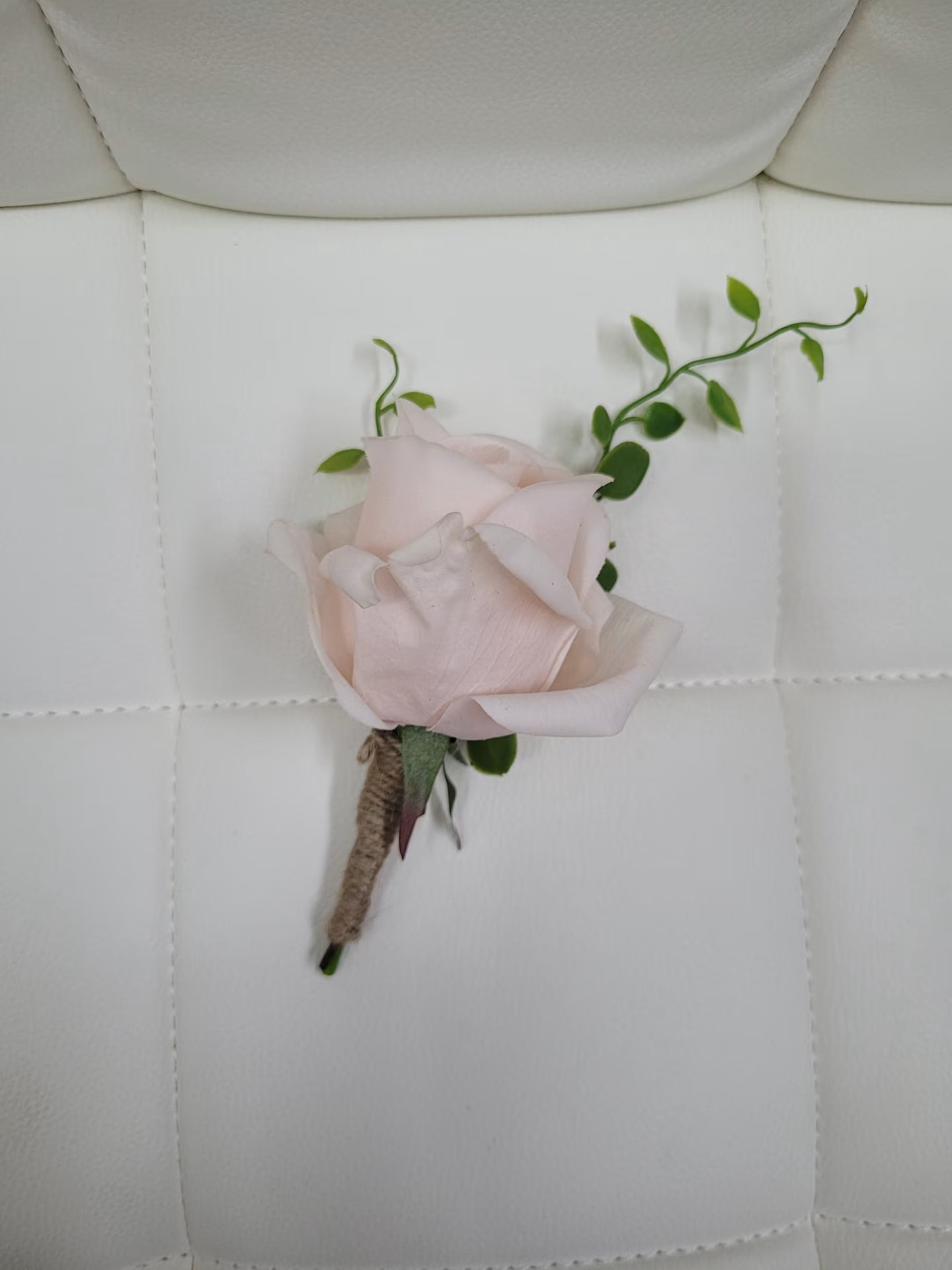 Pink rose boutonniere on a white quilted surface