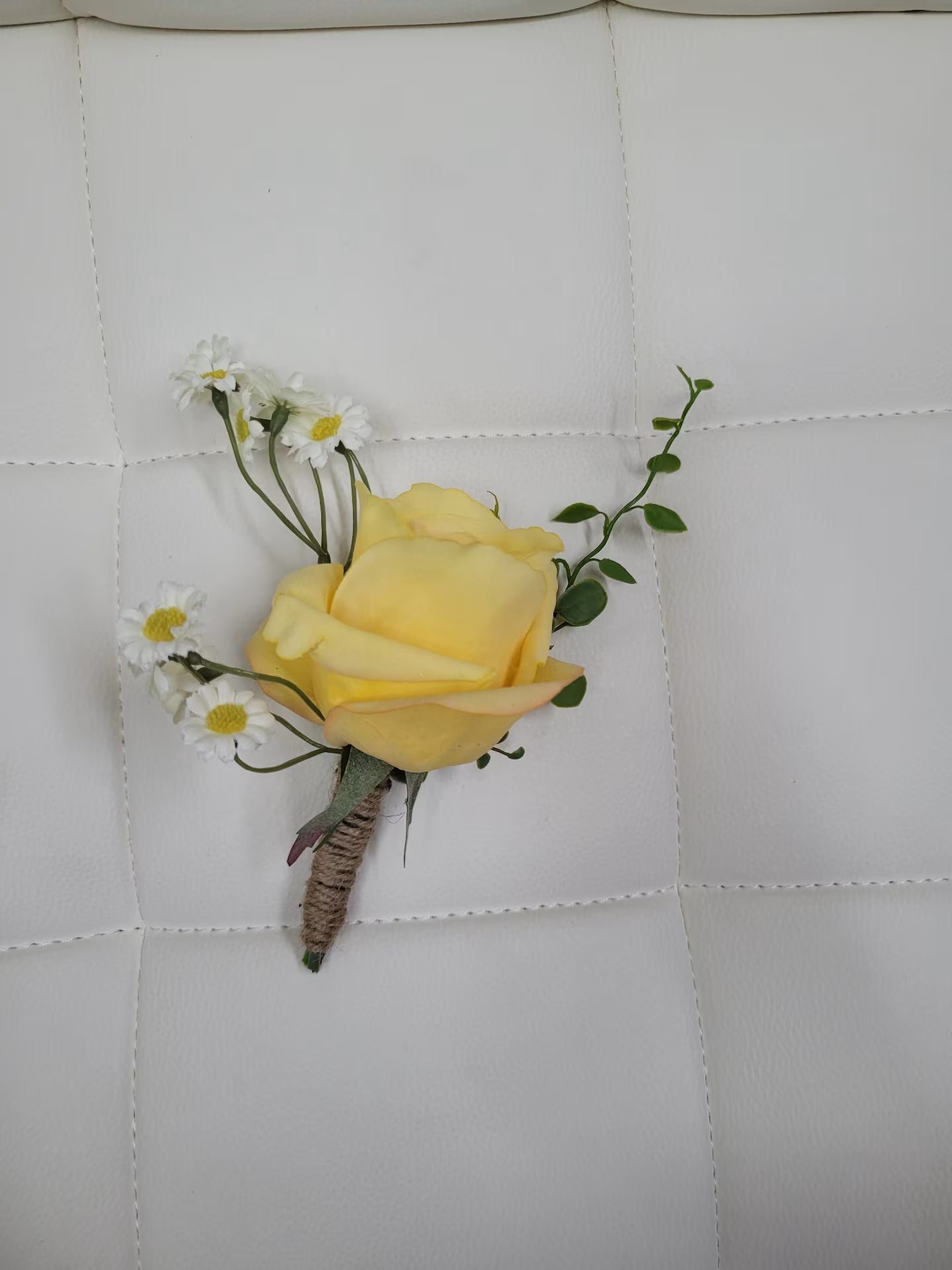Yellow rose boutonniere on a textured white surface