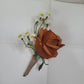 Floral boutonniere with a brown rose and white flowers on a white fabric background