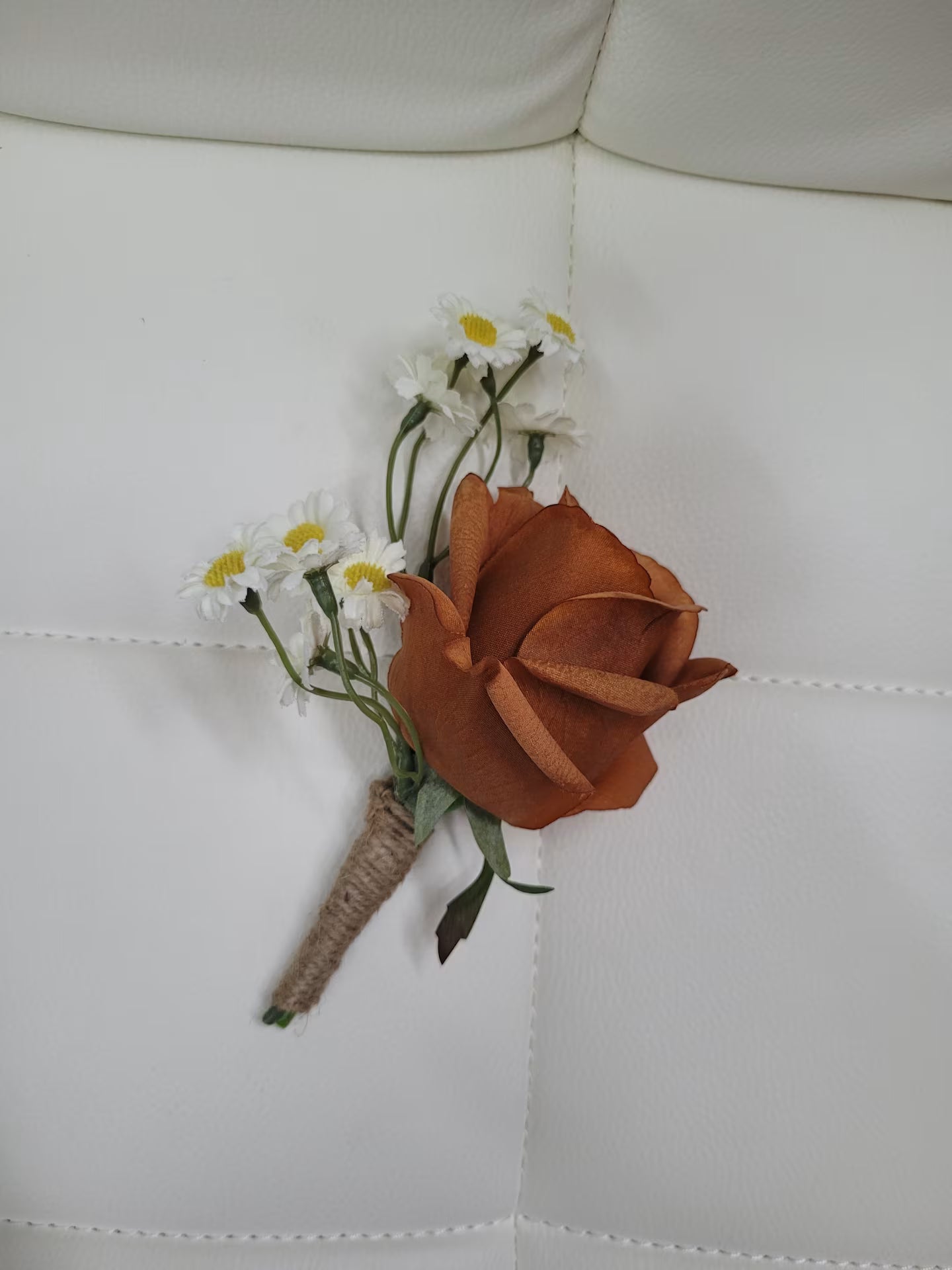 Floral boutonniere with a brown rose and white flowers on a white fabric background