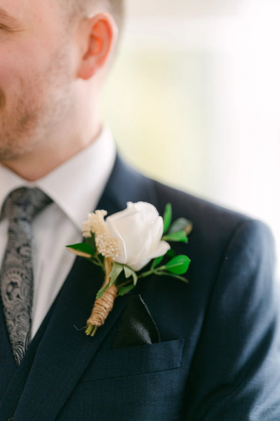Groom wearing a dark suit with a white rose boutonniere on a blurred background