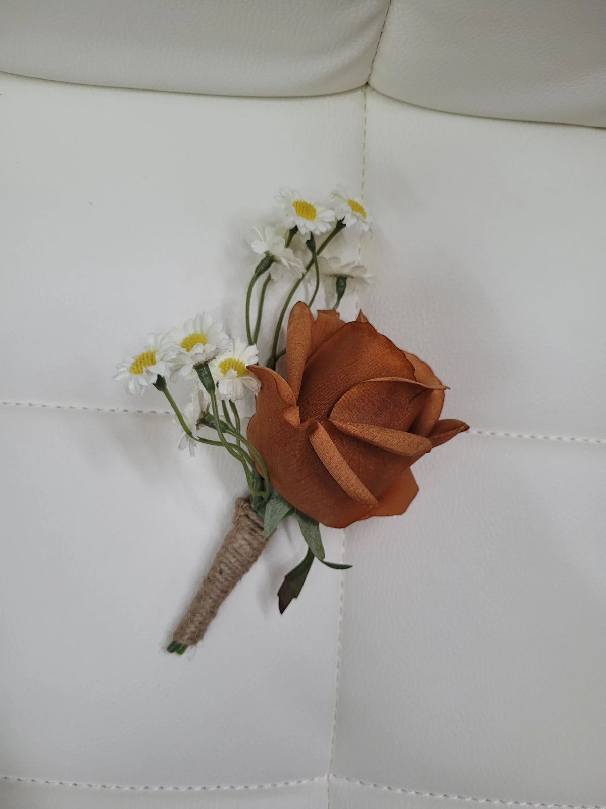 Floral boutonniere with orange rose and white daisies on a light gray background