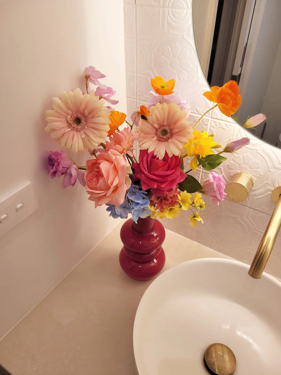 Colorful flowers in a pink vase on a bathroom counter next to a sink.