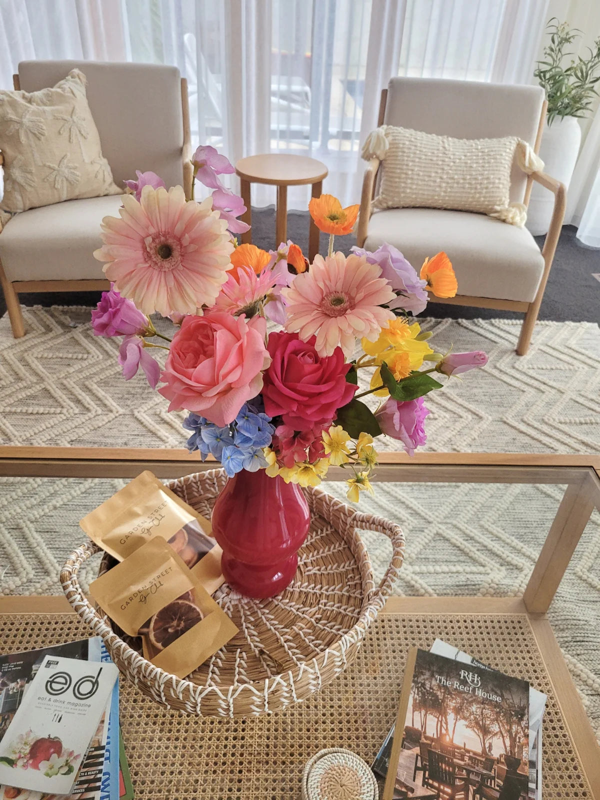 Colorful flowers in a red vase on a glass coffee table with a cozy living room setting.