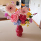 hot pink vase on a kitchen counter holding a bright flower arrangement with large gerberas
