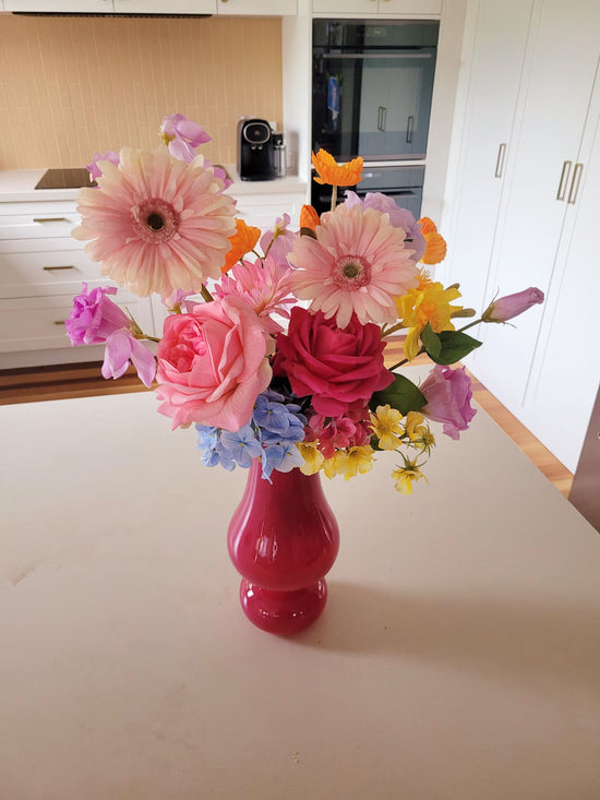 hot pink vase on a kitchen counter holding a bright flower arrangement with large gerberas