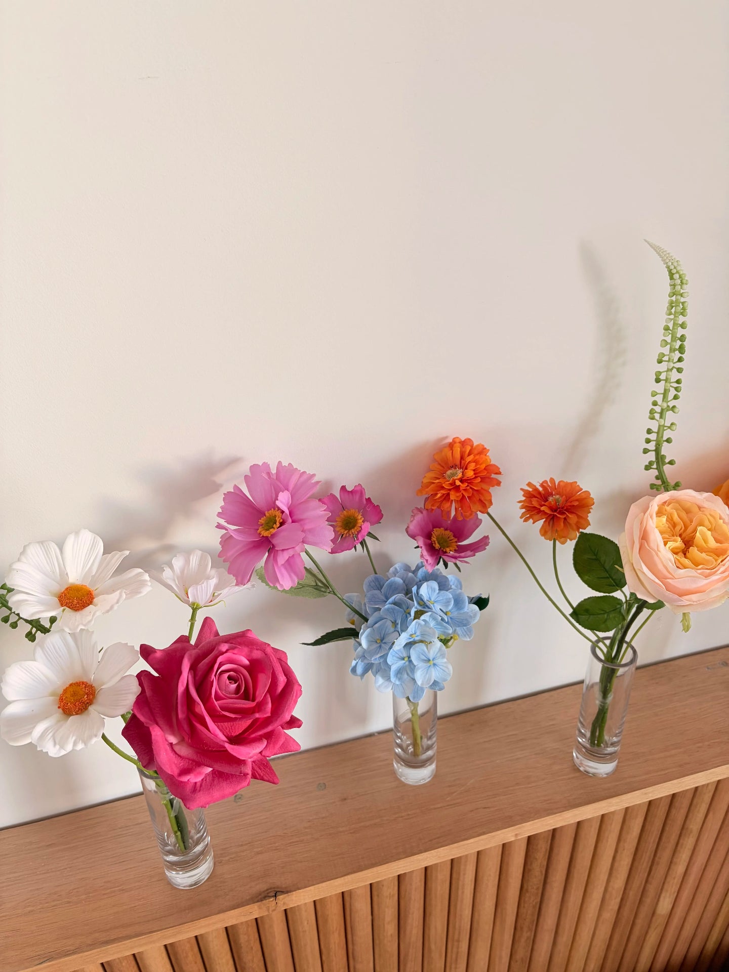 Bud vases with faux flowers on a wooden surface
