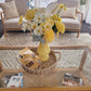 Yellow vase with flowers on a glass coffee table in a living room.