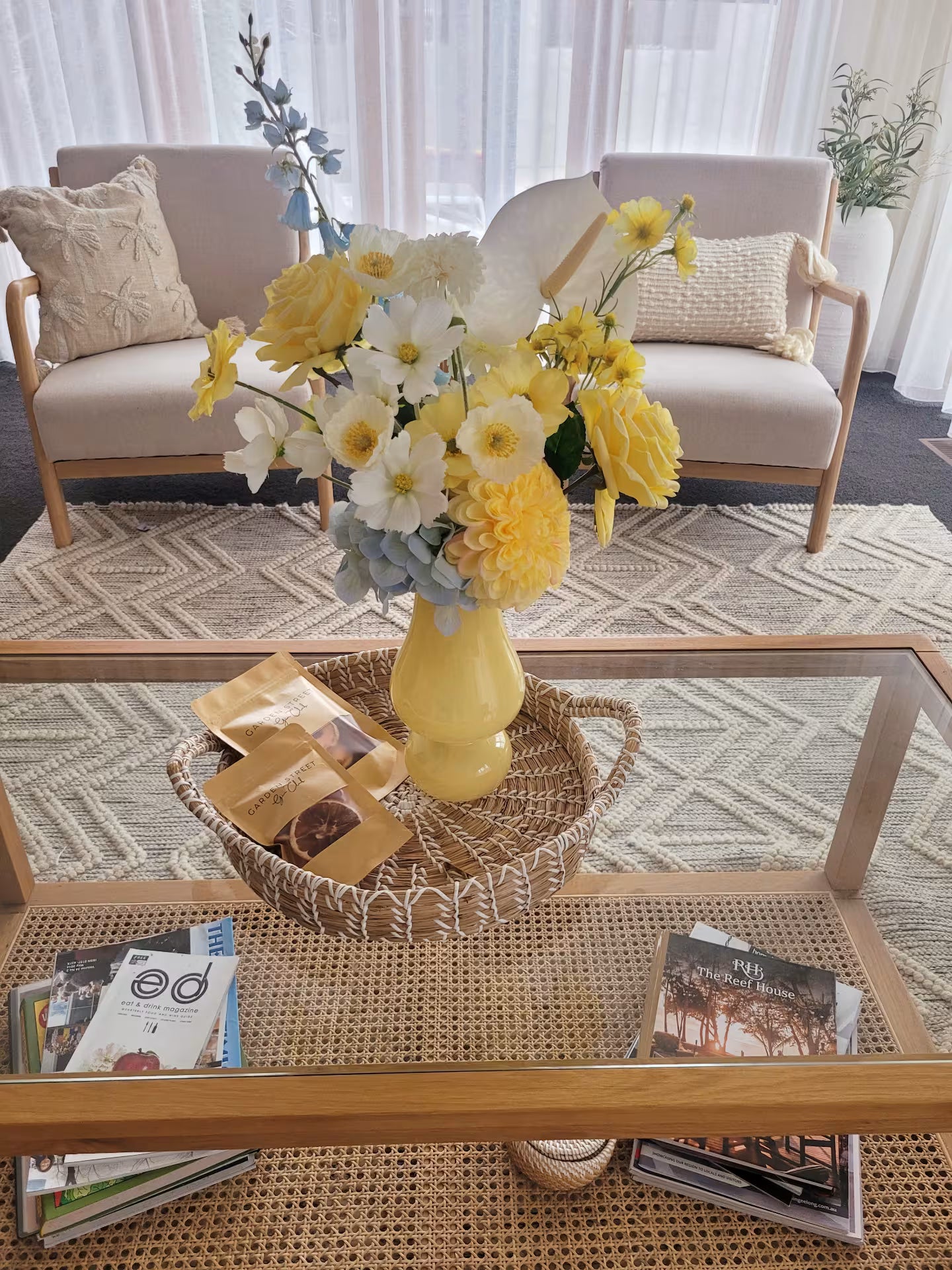 Yellow vase with flowers on a glass coffee table in a living room.